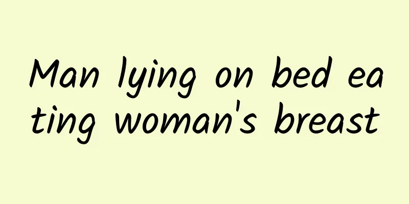 Man lying on bed eating woman's breast